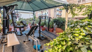 Un gimnasio al aire libre con equipo de ejercicio, incluyendo un banco, máquinas de pesas y una cinta de correr, bajo una cubierta sombreada.