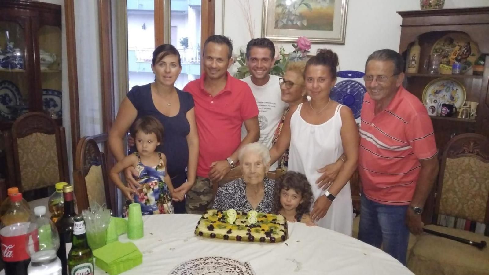 Un gruppo di persone riunito attorno a un tavolo con una torta, bottiglie e bicchieri.