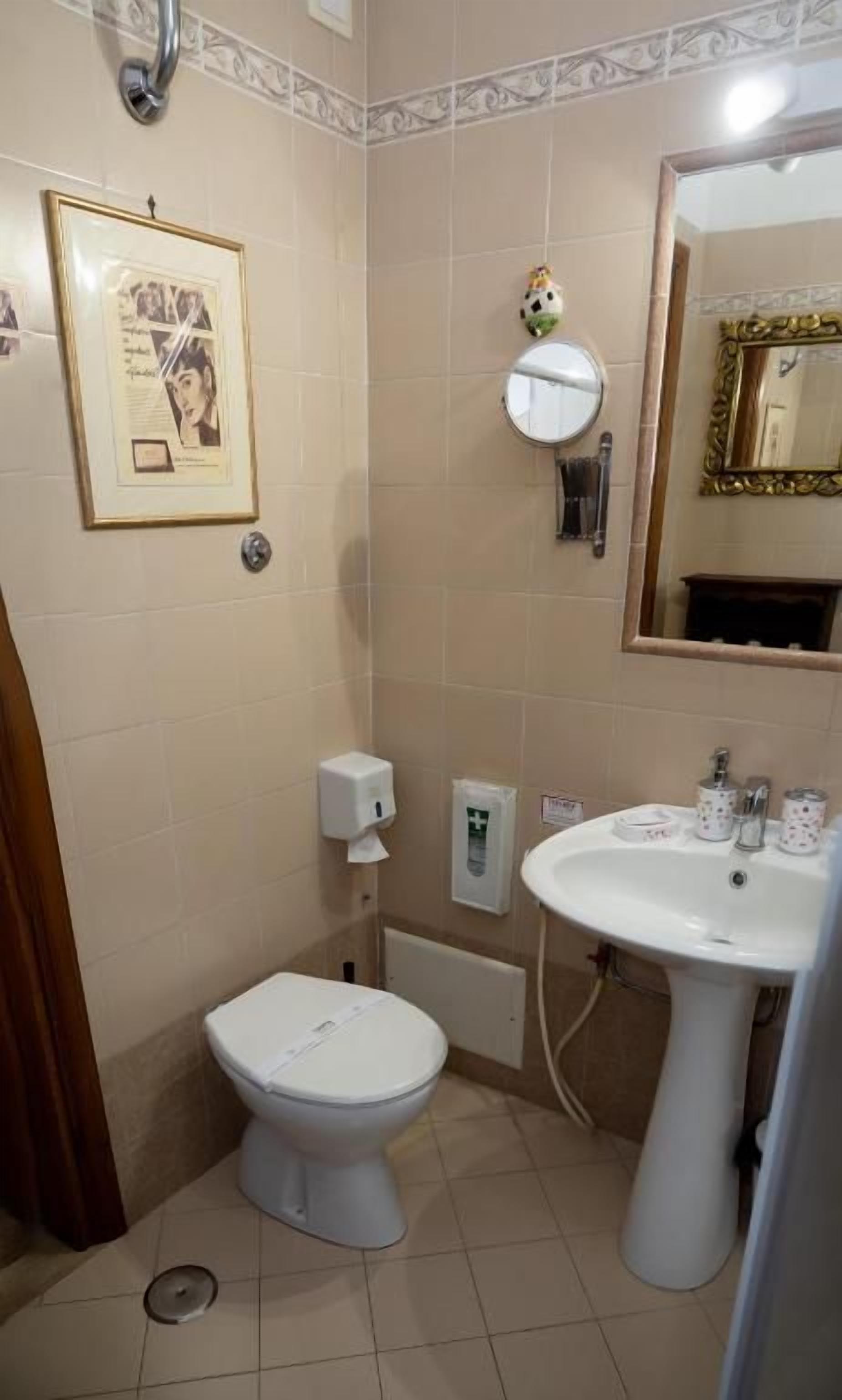 Et badeværelse med toilet, vask, spejl og et billede i ramme.