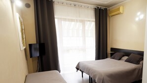 Una habitación de hotel con dos camas, un televisor de pantalla plana, un equipo de aire acondicionado y un ventanal con cortinas translúcidas.