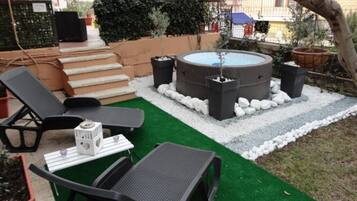 Un espacio al aire libre con un jacuzzi, sillones de descanso y una mesita con un altavoz.