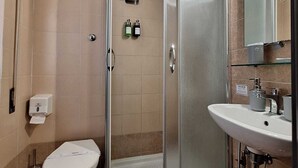 Un baño con ducha de vidrio, inodoro y lavamanos con espejo.