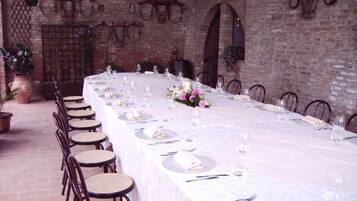 A long dining table set for a meal in a brick-walled room with chairs and potted plants.