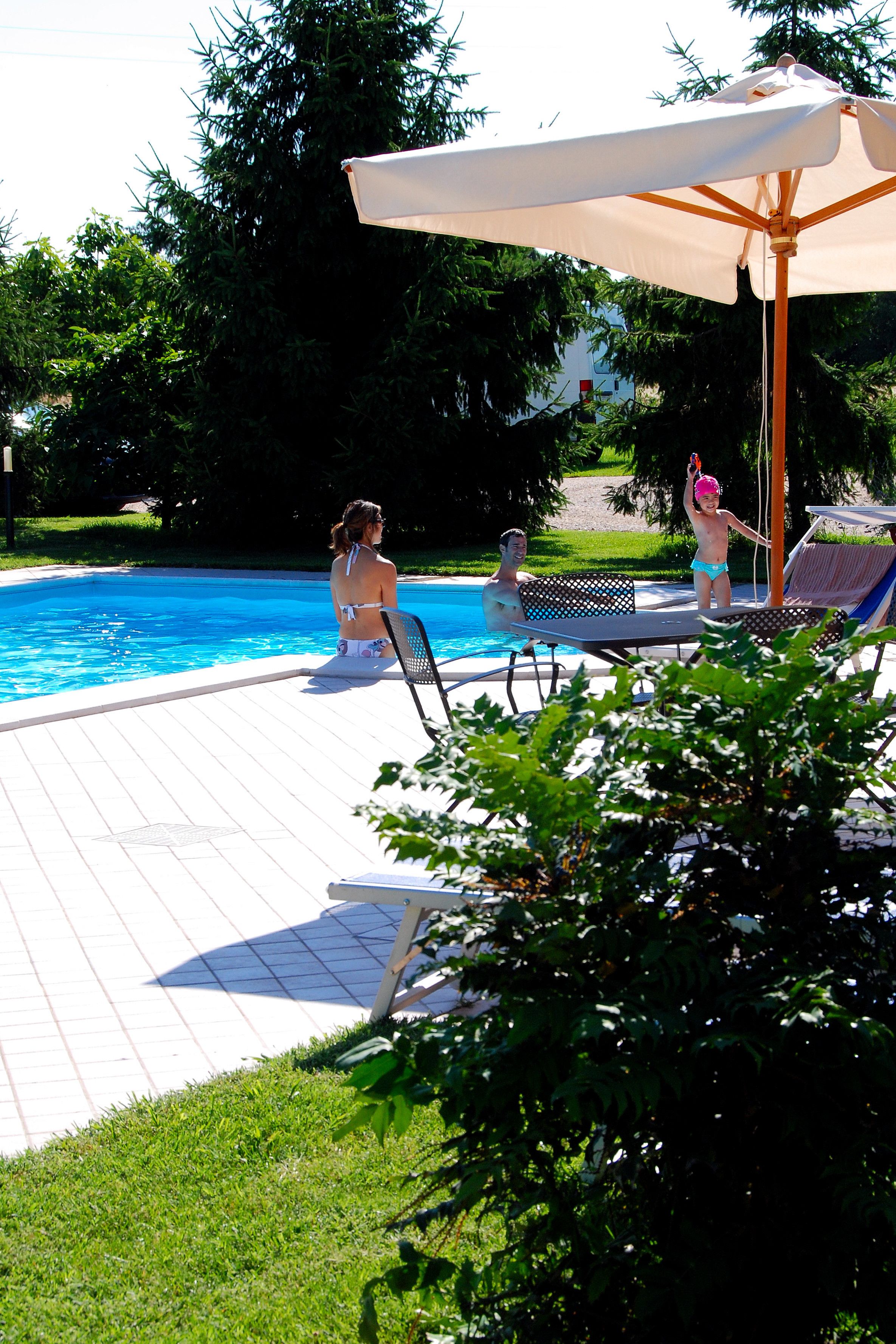 A swimming pool area with lounge chairs and an umbrella.