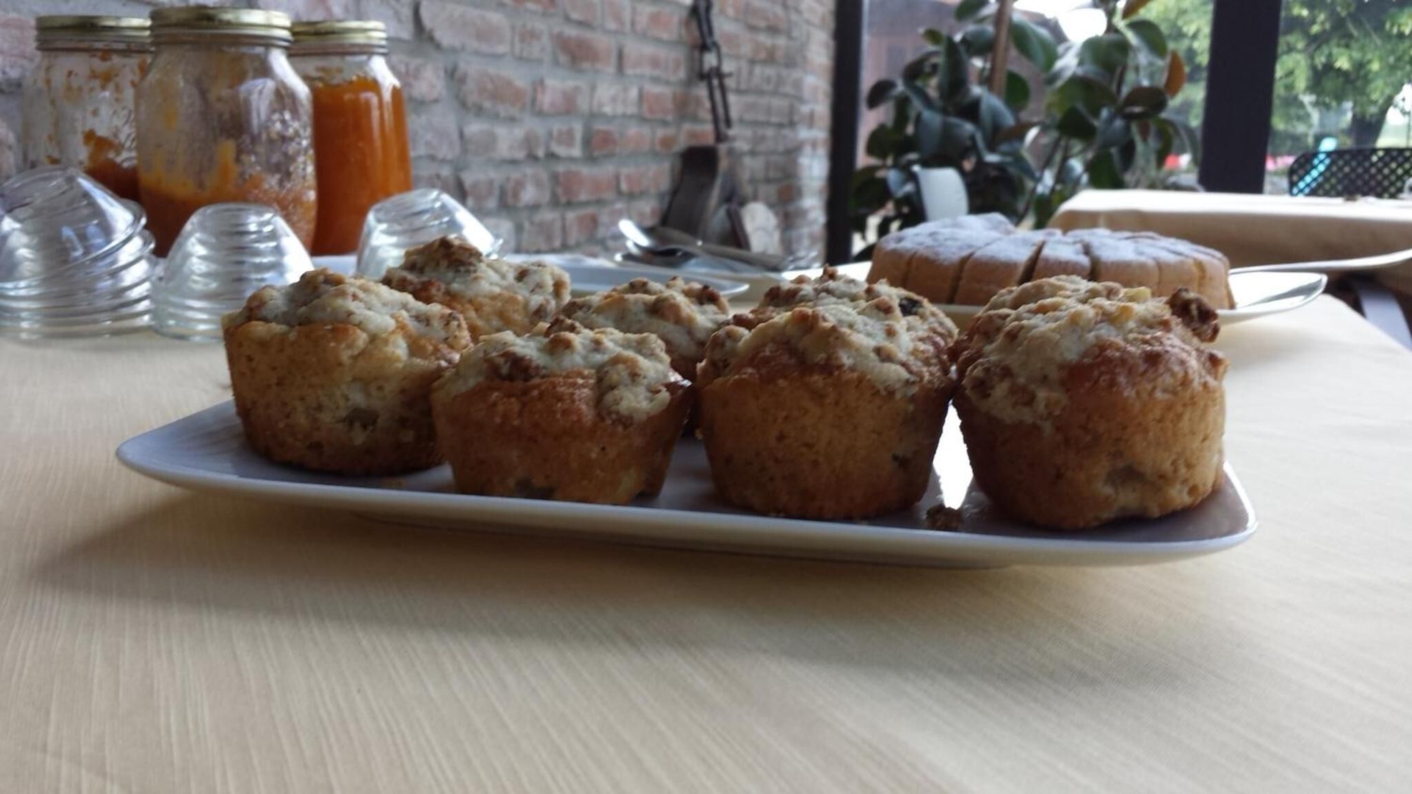 A plate of muffins on a table with jars of jam in the background.