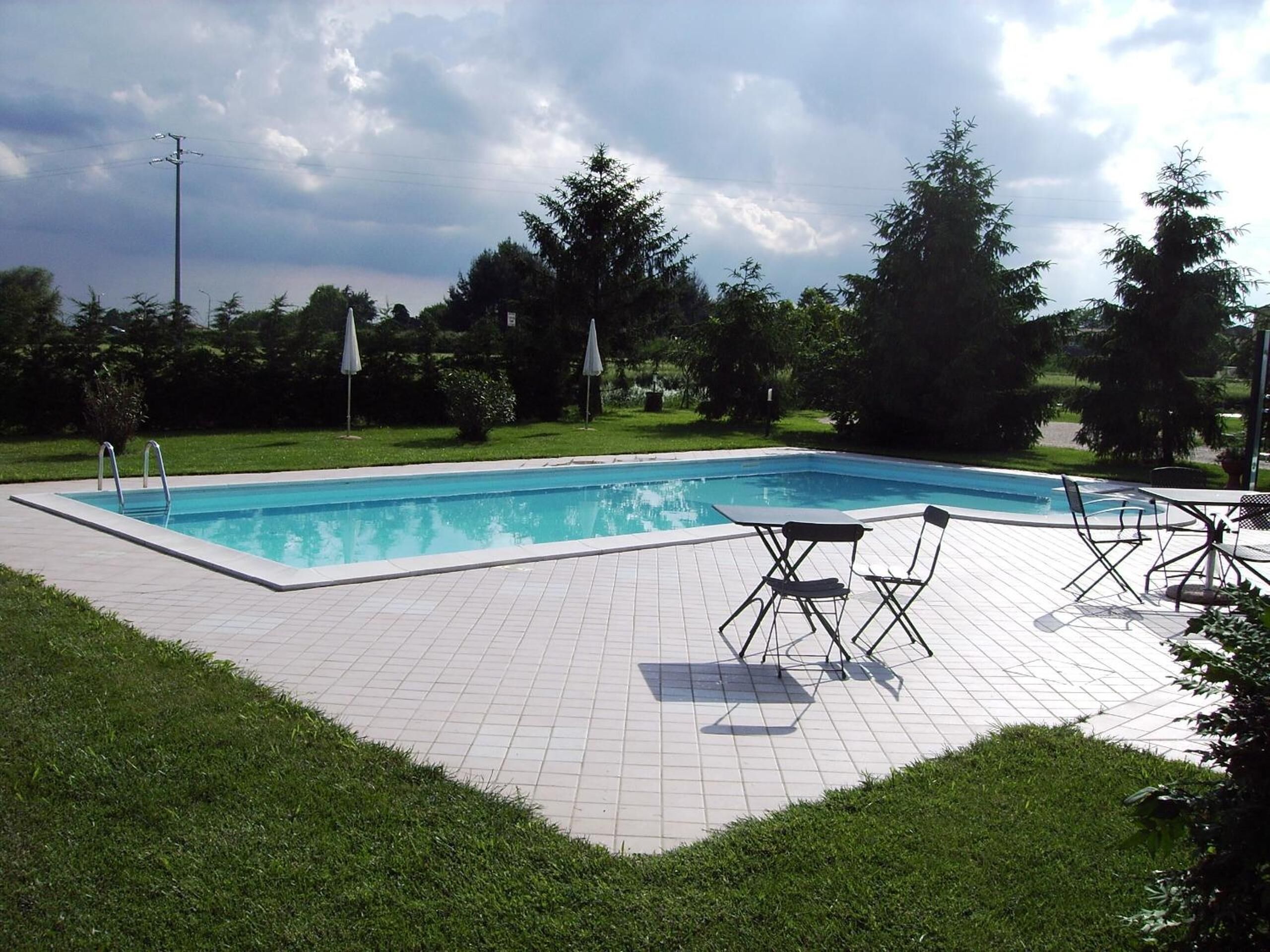 A rectangular swimming pool with a tiled deck, surrounded by grass and trees.