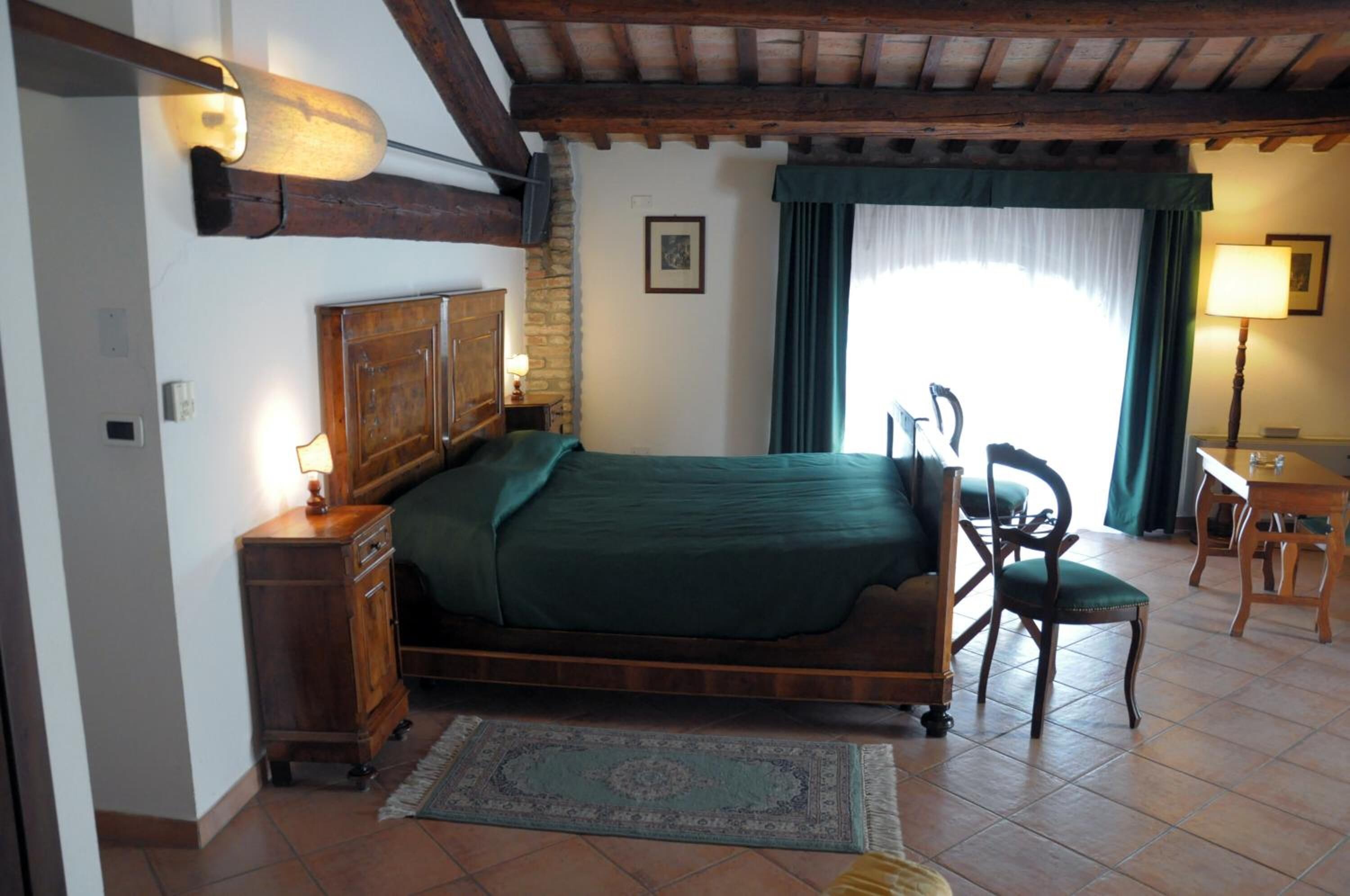 Ein Schlafzimmer mit einem hölzernen Bett, einem Nachttisch, einem Sessel, einem Schreibtisch und einem Fenster mit Vorhängen.
