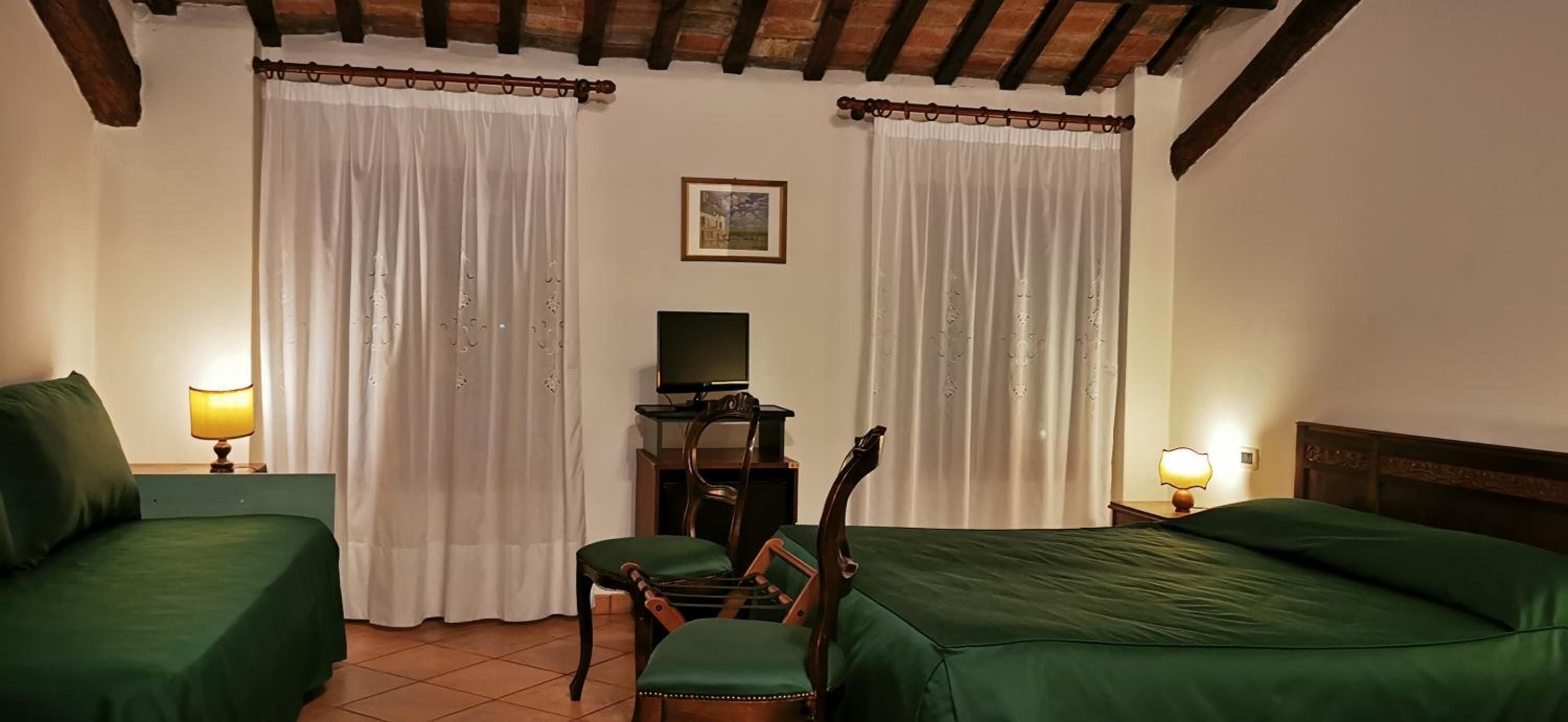A hotel room with two green beds, a desk with a television, a chair, and two lamps.
