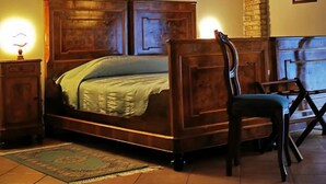 Un dormitorio con una cama de madera, una silla, una mesita de noche y una pared de piedra.