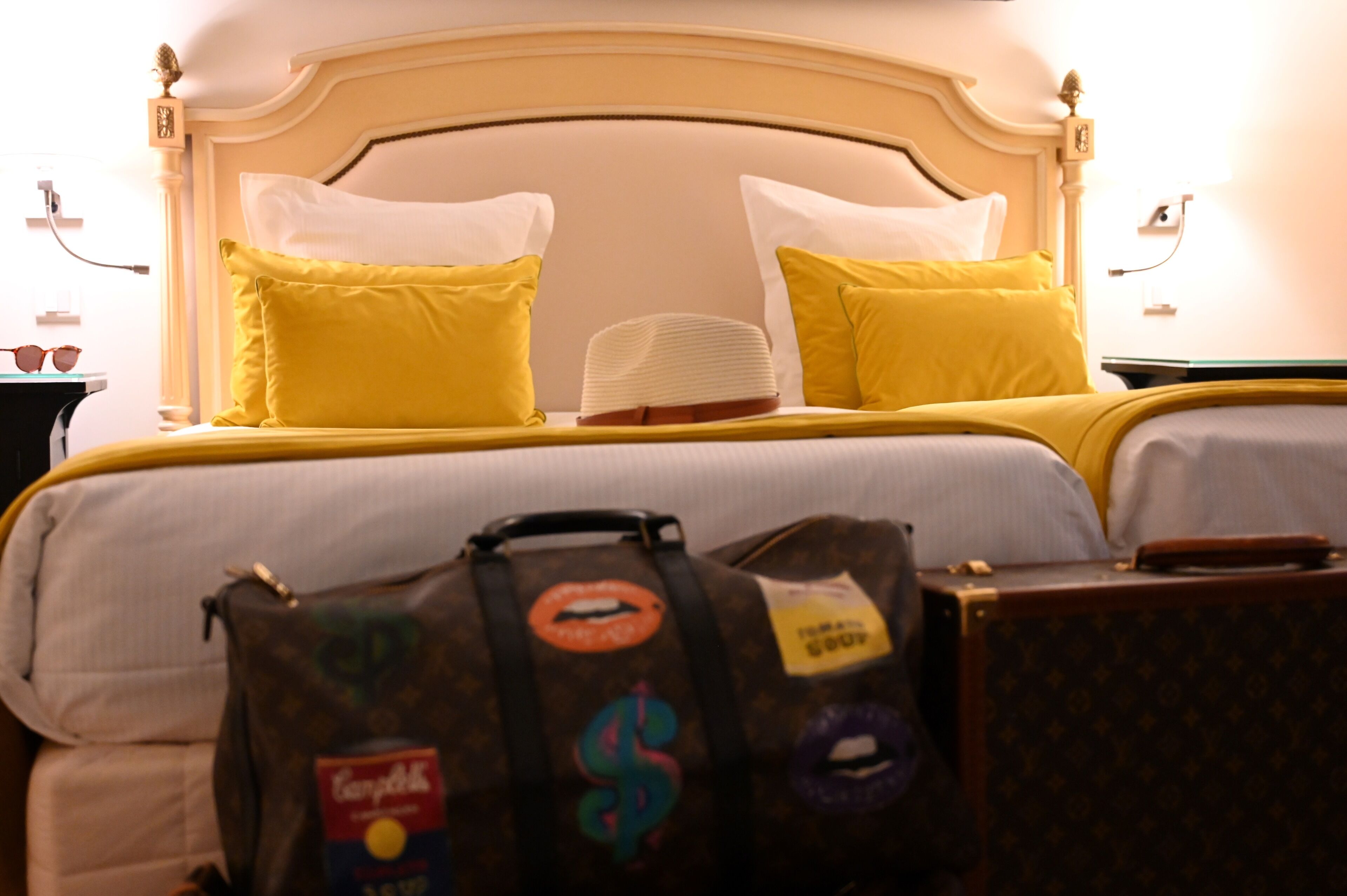 A hotel room with a bed, two pillows, a bedside table, and a suitcase.