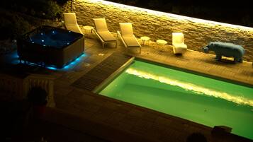 A hot tub with lounge chairs and a poolside area with a stone wall and a hippo statue.