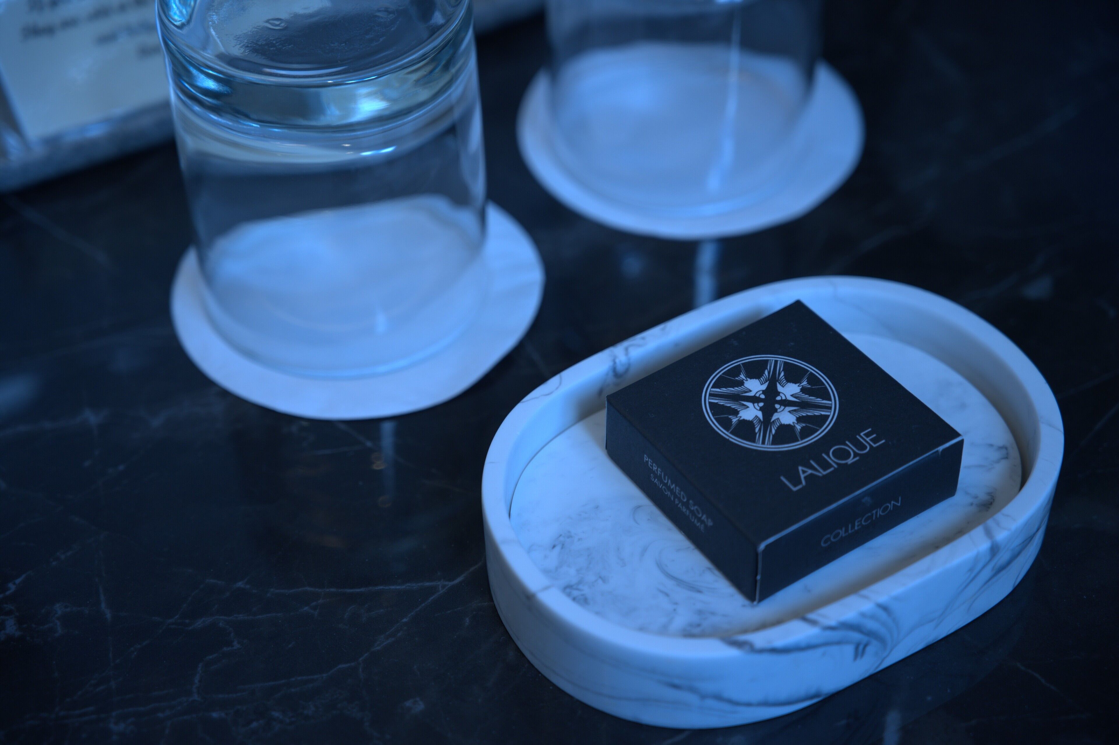 Una mesa de mármol con una caja negra que indica "Colección Lalique" y dos vasos de cristal.