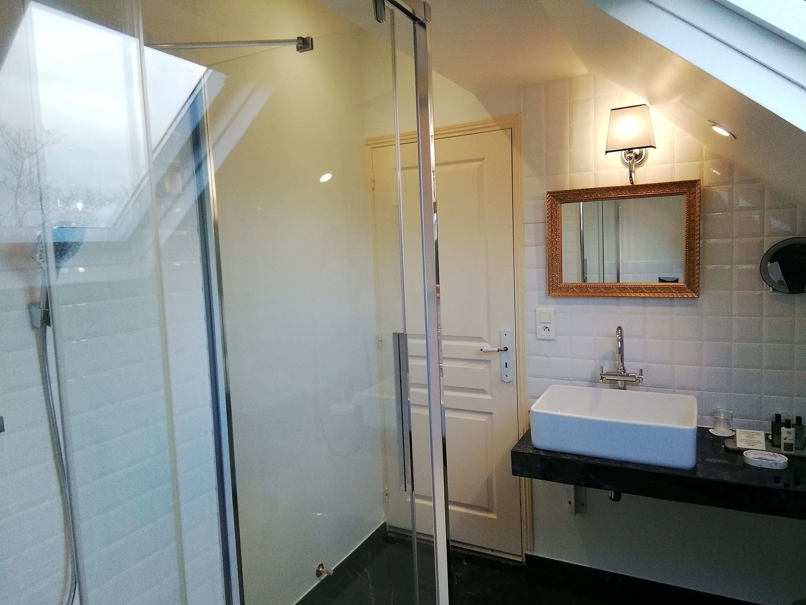 A modern bathroom with a glass shower enclosure, a white sink, and a mirror with a decorative frame.