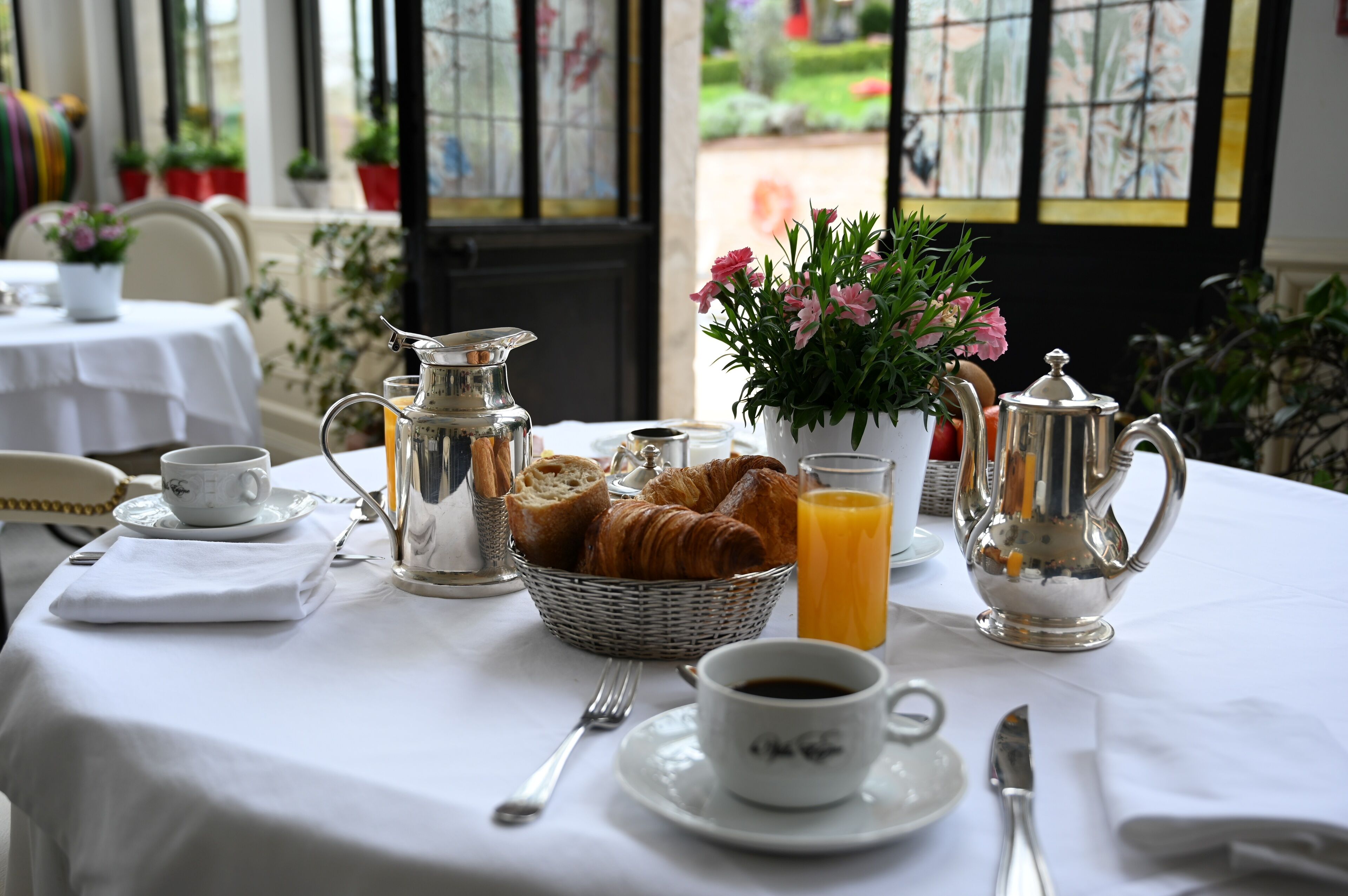 A breakfast table set with croissants, orange juice, coffee, and a pitcher.