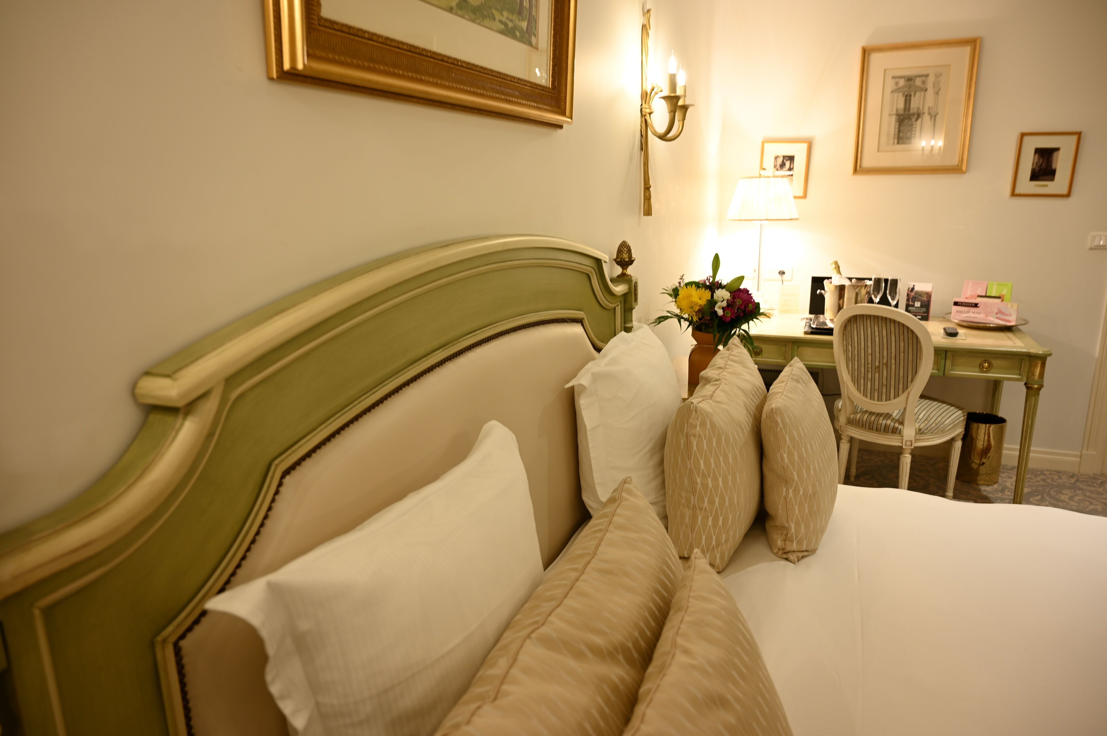 Una cama bien hecha con varias almohadas y un cabecero verde. Junto a la cama, un escritorio con una lámpara y una silla.