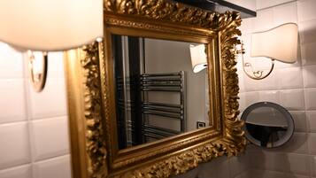Een badkamer met een spiegel met gouden lijst, een handdoekhouder, een wandlamp en een ronde spiegel.