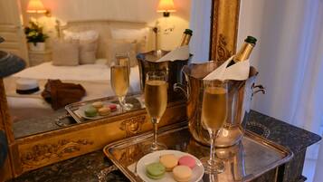 A tray with champagne glasses and macarons, a bottle of champagne, and a mirror reflecting a bed and a nightstand with a lamp.