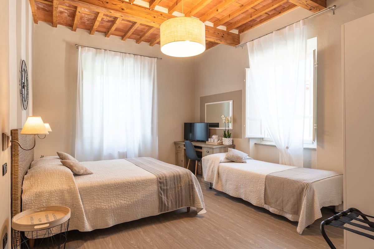 A bedroom with two beds, a desk, a television, and a window with curtains.
