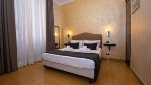 Quarto de hotel com cama grande, duas mesas de cabeceira, um criado-mudo, um espelho e luminária na parede.