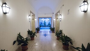 Um corredor com plantas em vasos, luminárias na parede e vista para o exterior.