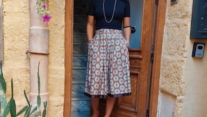 A woman standing at the entrance of a building with a patterned tiled staircase, a potted plant, and a wooden door. - Camere a Sud (Agrigento)