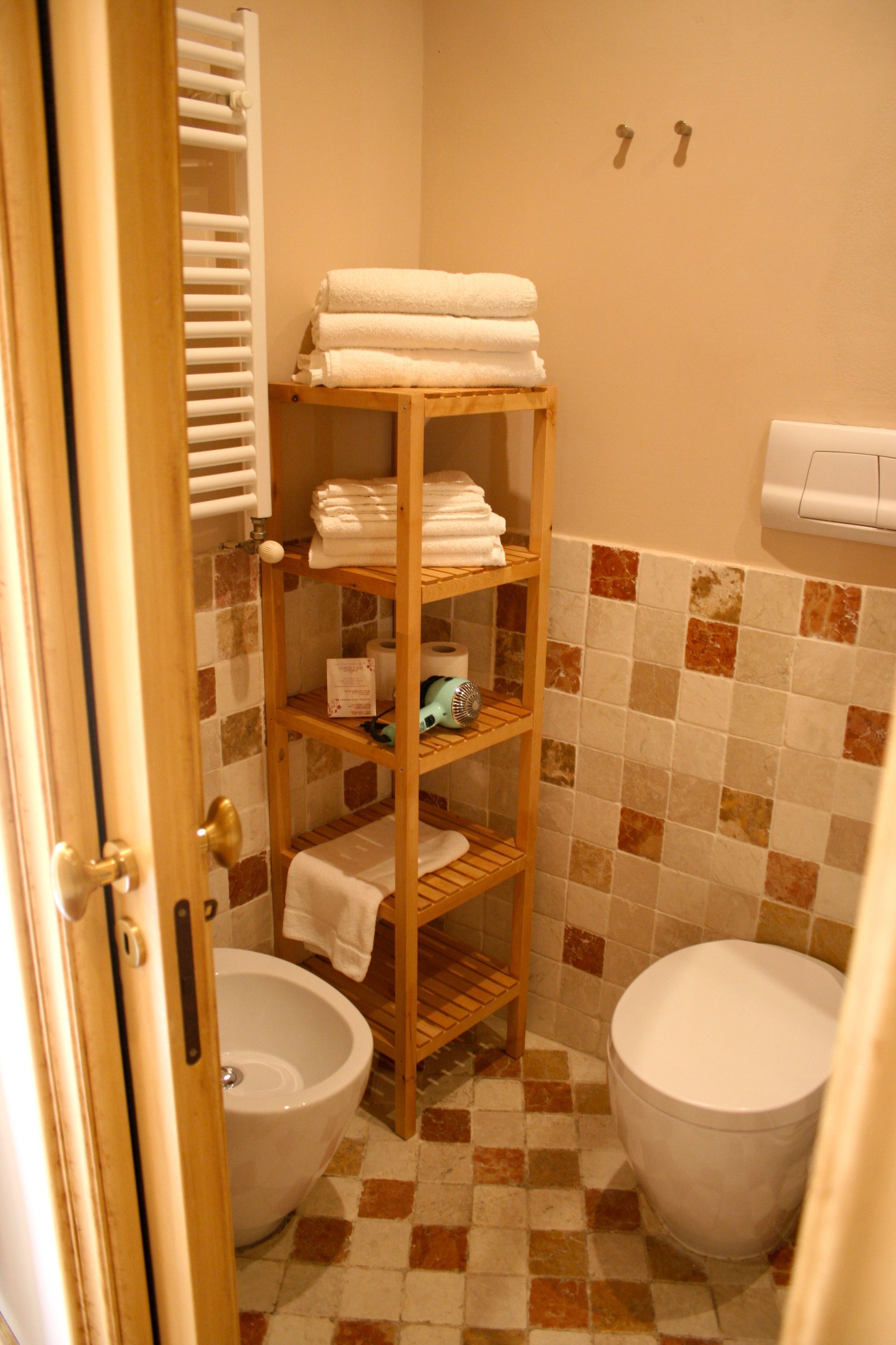 A bathroom with a tiled floor, a wooden shelf with towels, a toilet, and a bidet.
