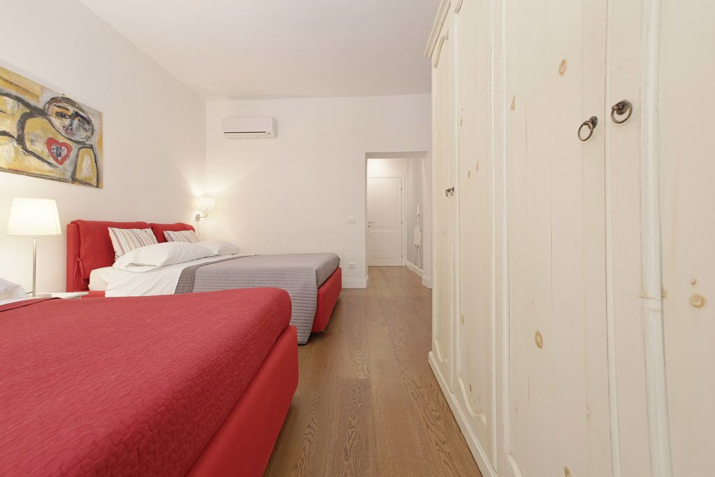 A hotel room with two beds, a painting on the wall, an air conditioning unit, and a wardrobe.