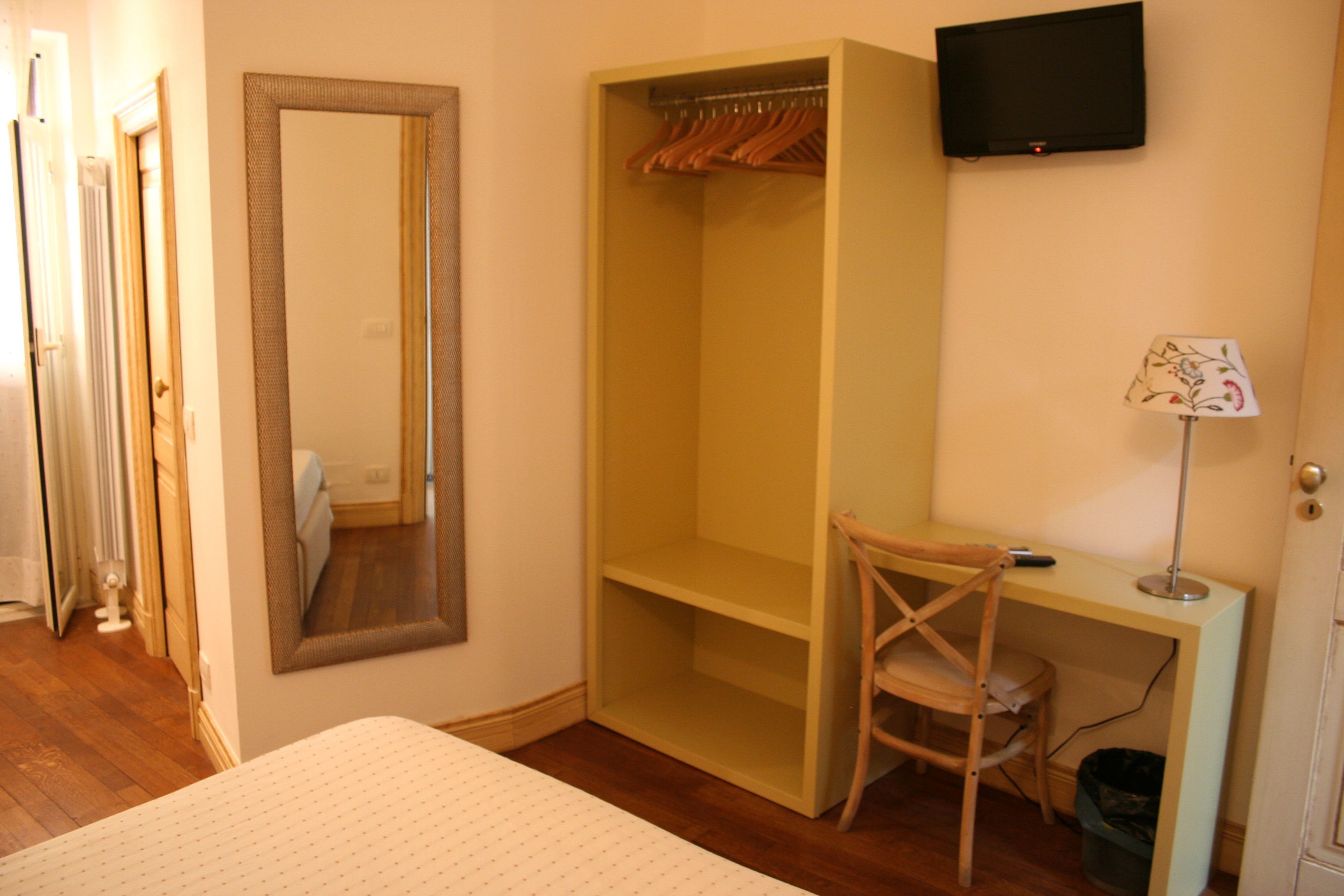 Un dormitorio con cama, armario, escritorio con silla, televisor y lámpara.