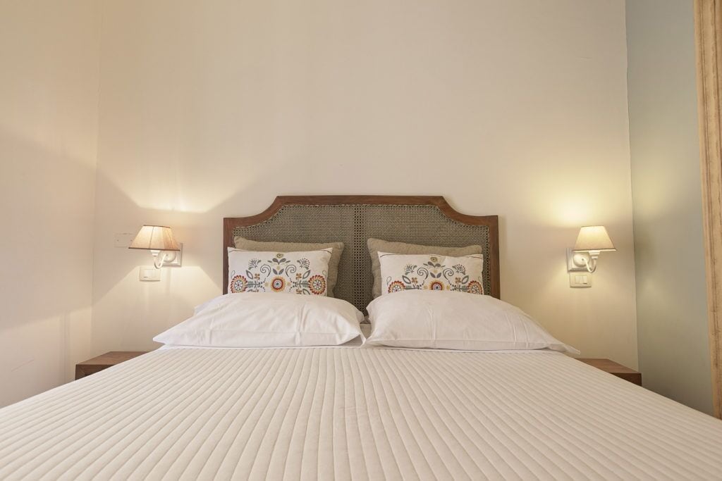 A neatly made bed with a wooden headboard and two decorative pillows, flanked by wall-mounted lamps.