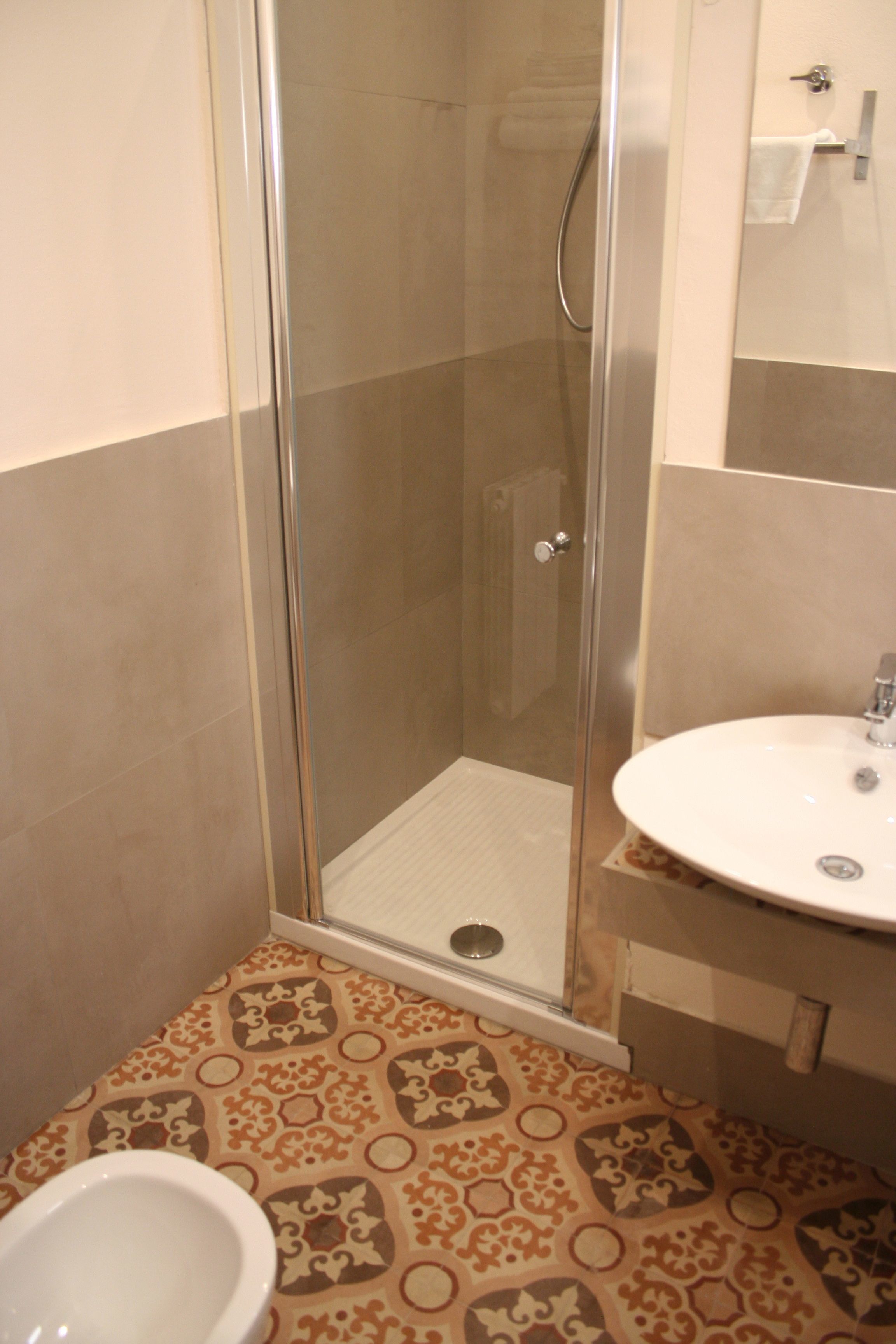 Casa de banho com cabine de duche em vidro, lavatório branco e ladrilhos com padrão.