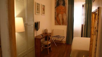 Una habitación con un escritorio de madera, una silla, una lámpara, un radiador, un cuadro y una cama.