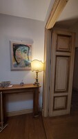 Una habitación con un escritorio de madera, una lámpara, un cuadro en la pared y una puerta.