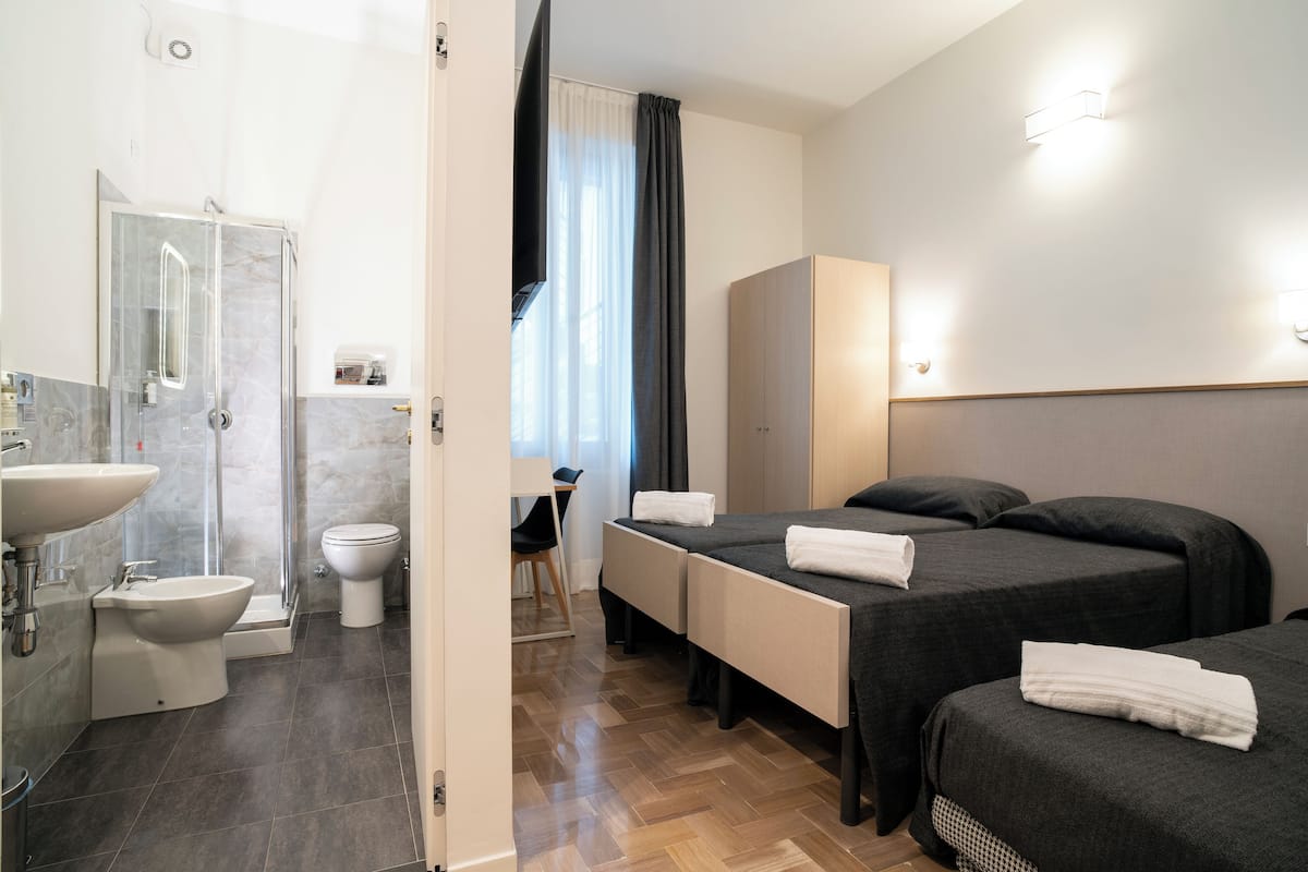 A hotel room with a shower, toilet, sink, and two beds.