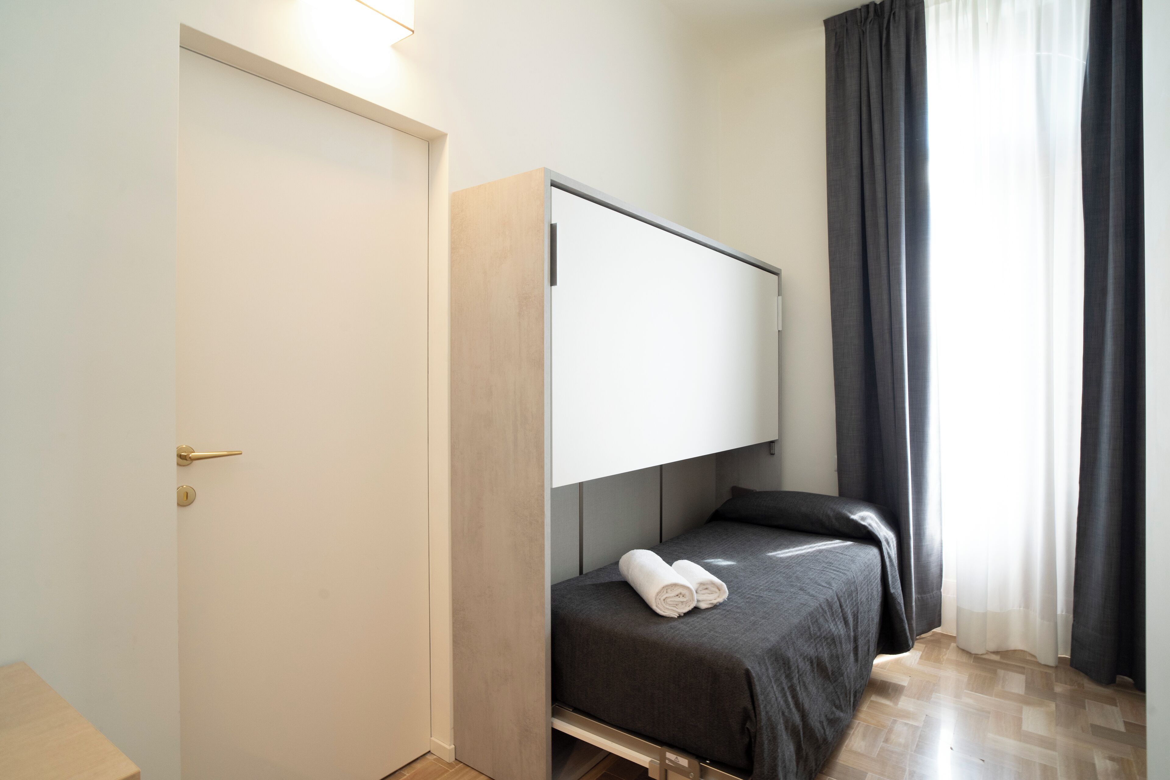Ein kleines Zimmer mit Bett, Kleiderschrank und einem fenster mit Vorhängen.