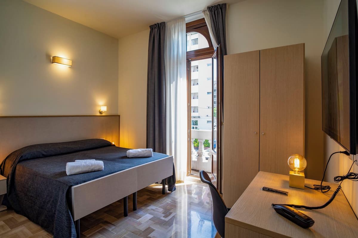 A hotel room with a bed, bedside table, desk, chair, and a TV.