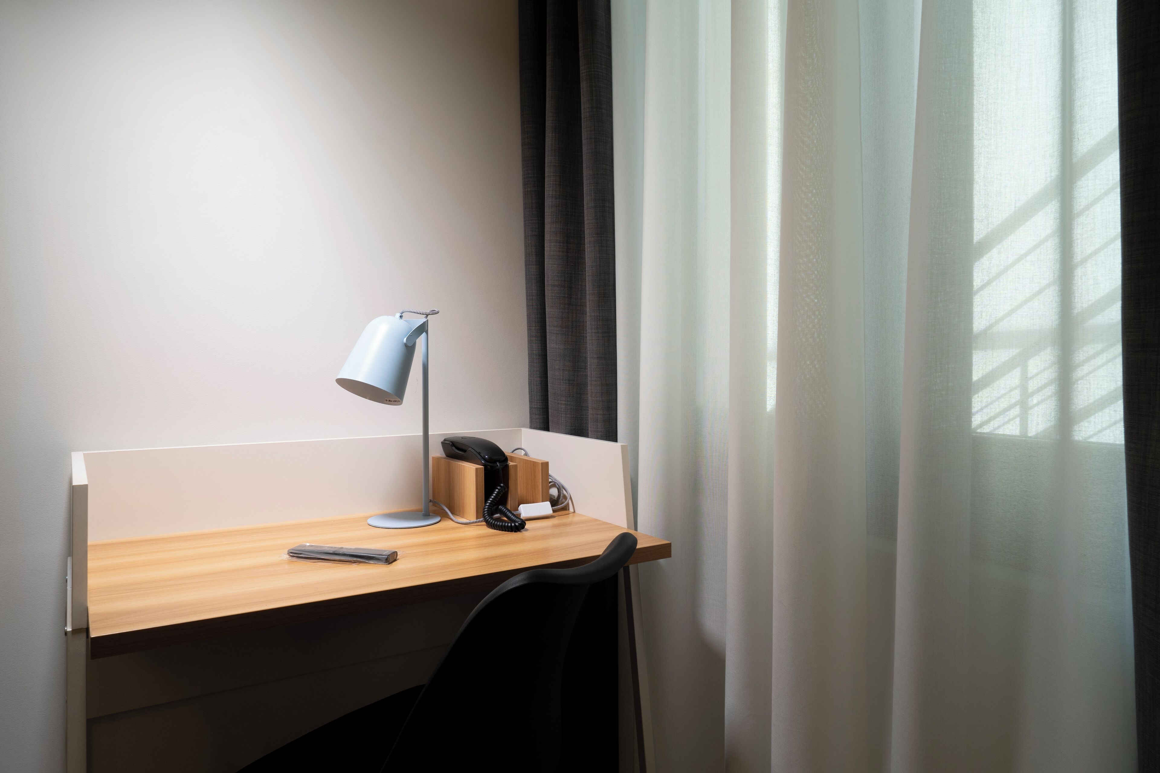 Espacio de trabajo en un hotel, con escritorio, lámpara de escritorio, teléfono y silla.