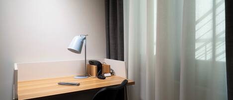 A hotel workspace with a desk, a desk lamp, a telephone, and a chair.