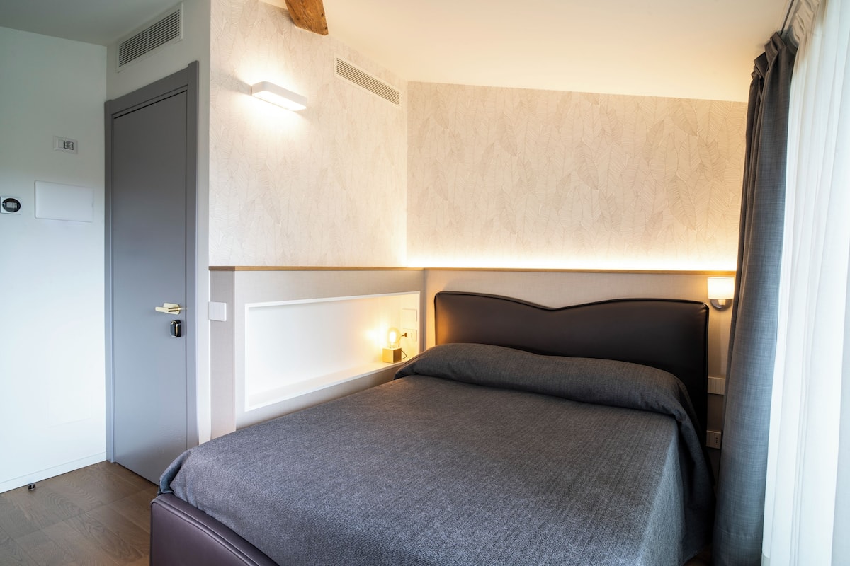 A hotel room with a bed, bedside lamps, a door, and a window with curtains.