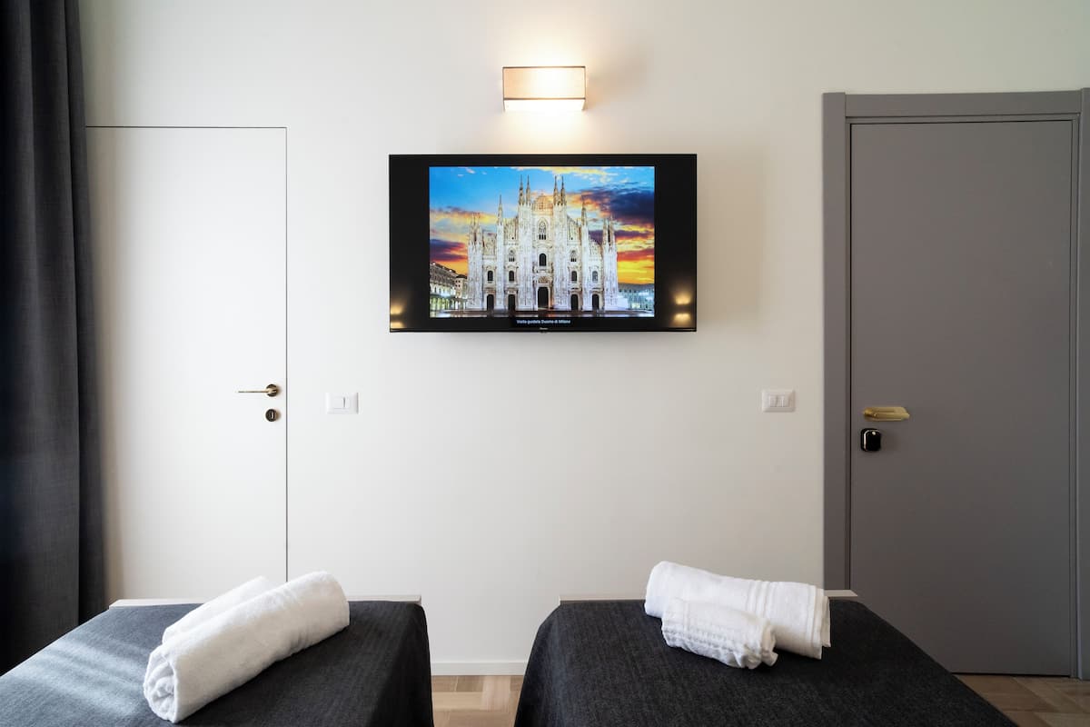 A hotel room with two beds, a TV mounted on the wall displaying a cathedral, and a door to the right.