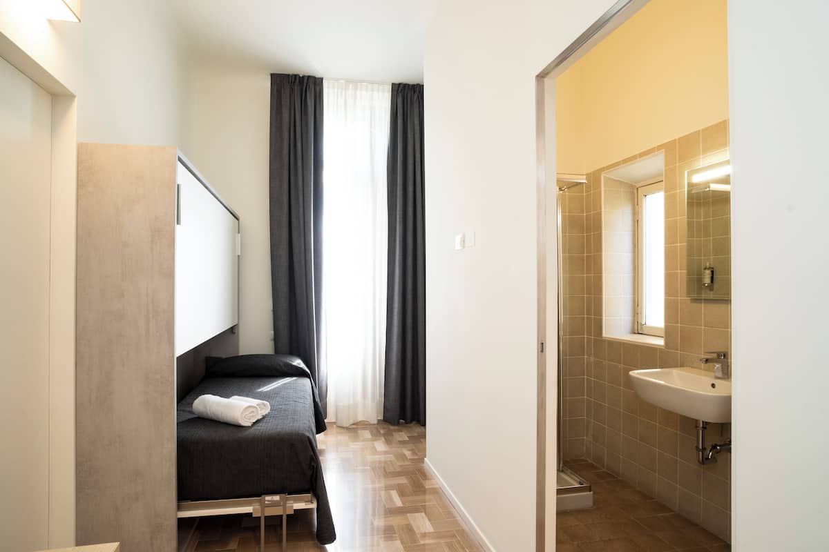 A modern hotel room with a bed, a bathroom with a sink, and a window with curtains.