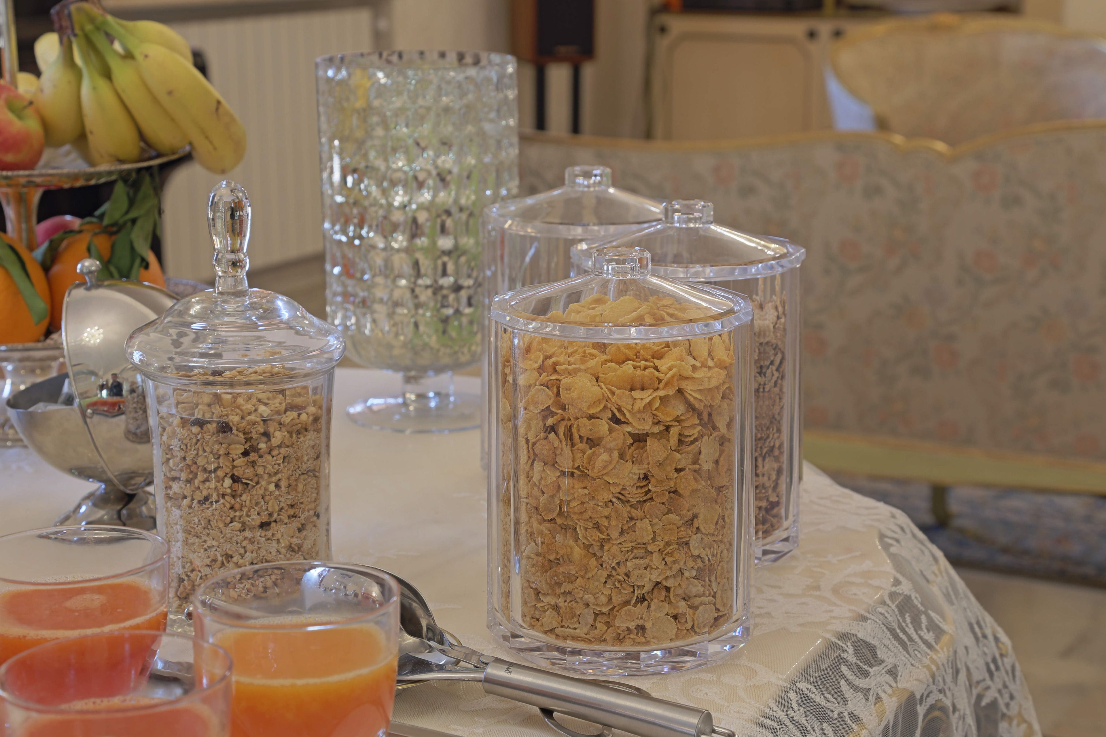 A breakfast table with cereal containers, a fruit bowl, and glasses of orange juice.