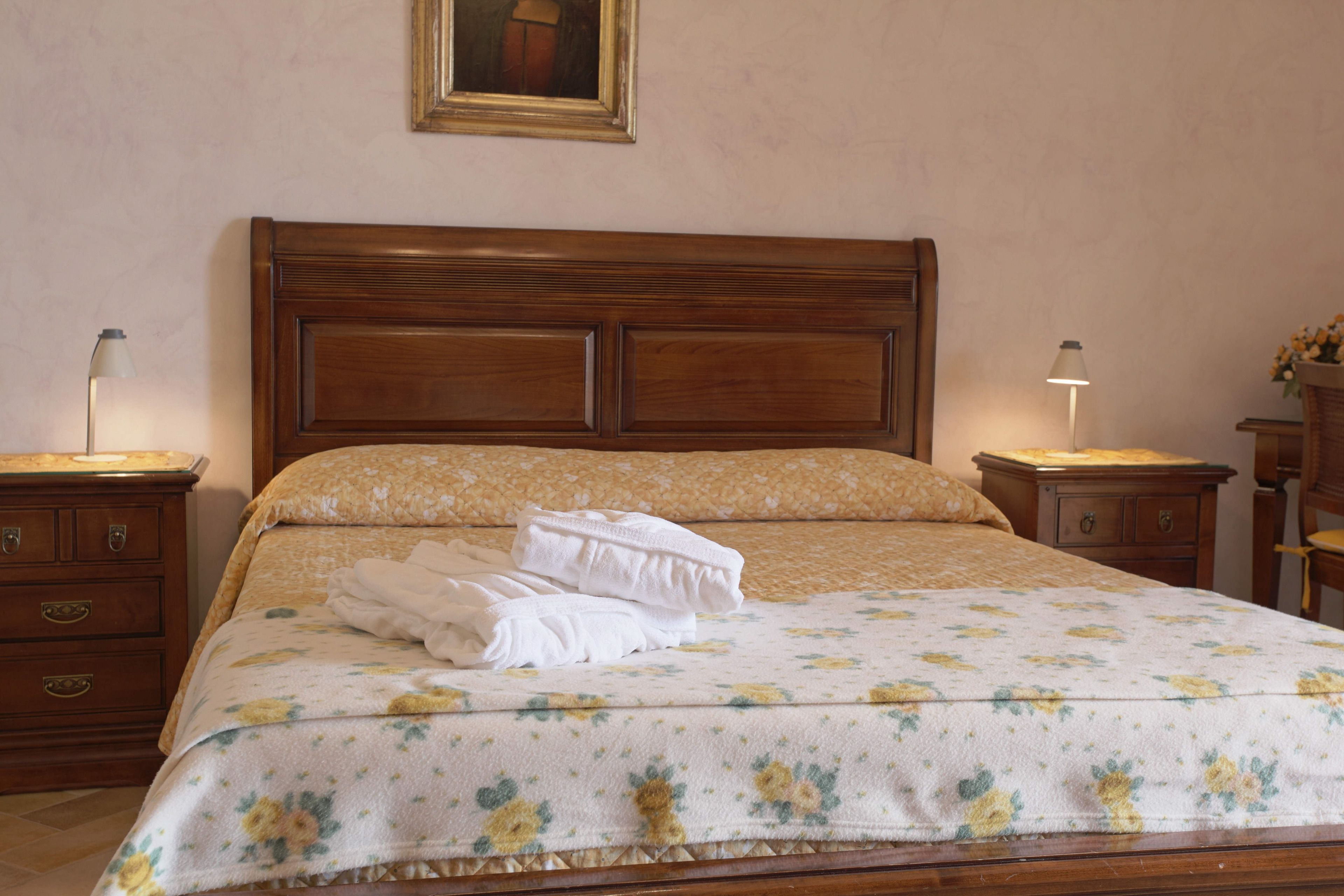 A neatly made bed with a floral bedspread, wooden headboard, and two bedside tables with lamps.