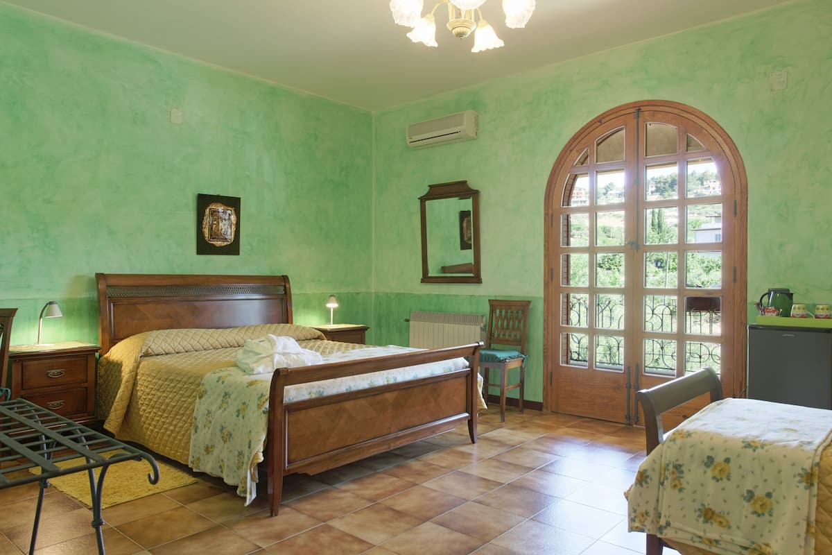 A bedroom with a wooden bed, a chair, a table, and a large arched window.
