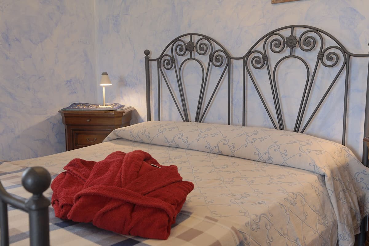 A neatly made bed with a patterned bedspread, a red bathrobe on the bed, and a bedside table with a lamp.