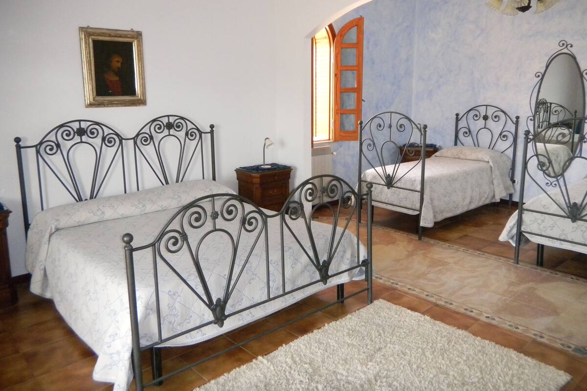 A bedroom with two metal-framed beds, a wooden nightstand, a small table, and a mirror.