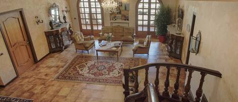A spacious living room with a large rug, leather sofas, a coffee table, and a staircase leading to an upper floor.