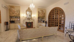 Un salon spacieux doté d’un sol en marbre, d’un grand canapé, d’une cheminée ornée d’une guirlande et d’une bibliothèque remplie de livres.