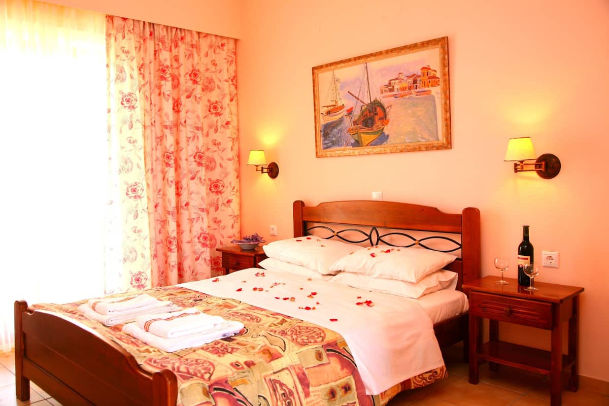 A neatly made bed with a floral bedspread, a wooden headboard, and a nightstand with a bottle and glass.