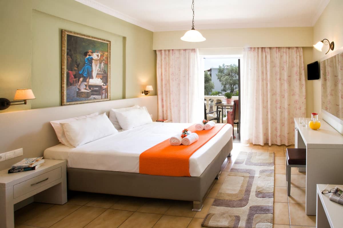 A hotel room with a bed, a desk, a chair, a painting on the wall, and a view of the outside.