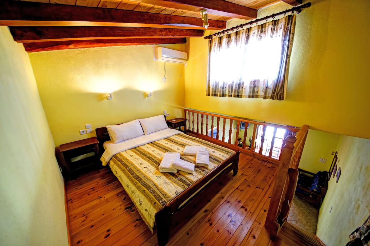 A wooden-floored bedroom with a bed, nightstands, and an air conditioning unit.